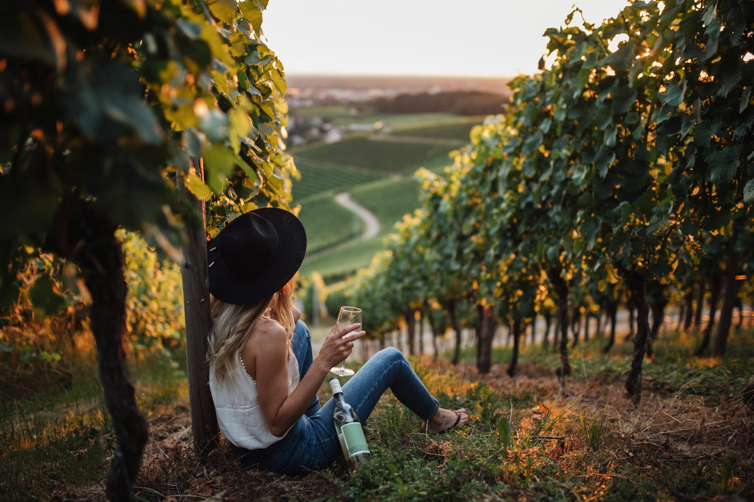 young-blonde-woman-relaxing-vineyards-summer-season-with-bottle-wine-scaled